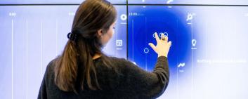 A woman stands in front of a big touchscreen.