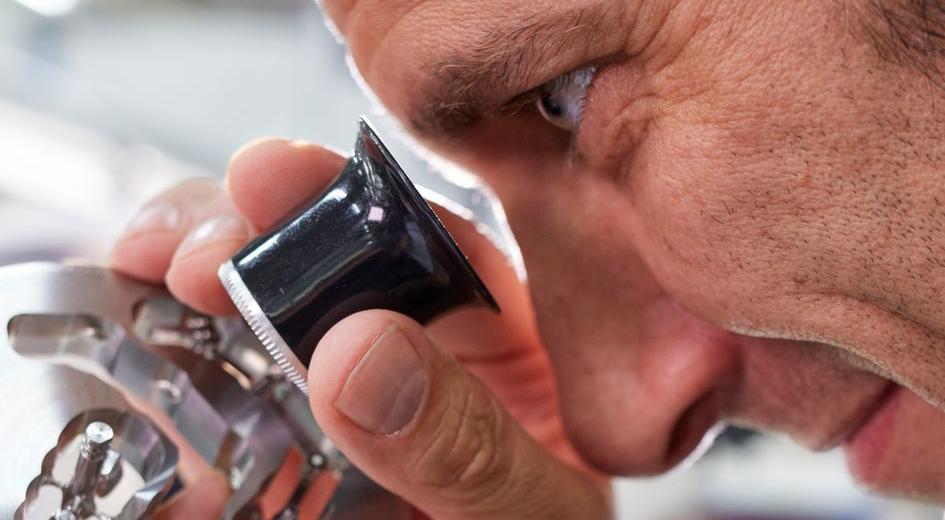 Un uomo osservare un pezzo di metallo con la lente d’ingrandimento.