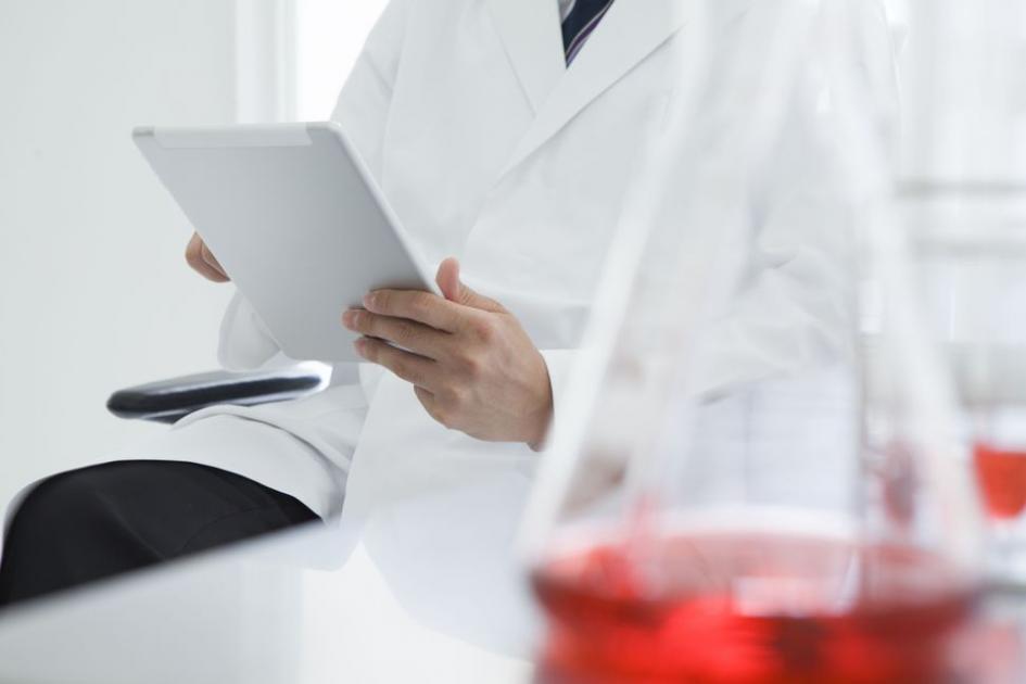 A man in a lab coat holds an iPad