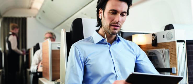 A man with headphones and a tablet is sitting in an airplane.
